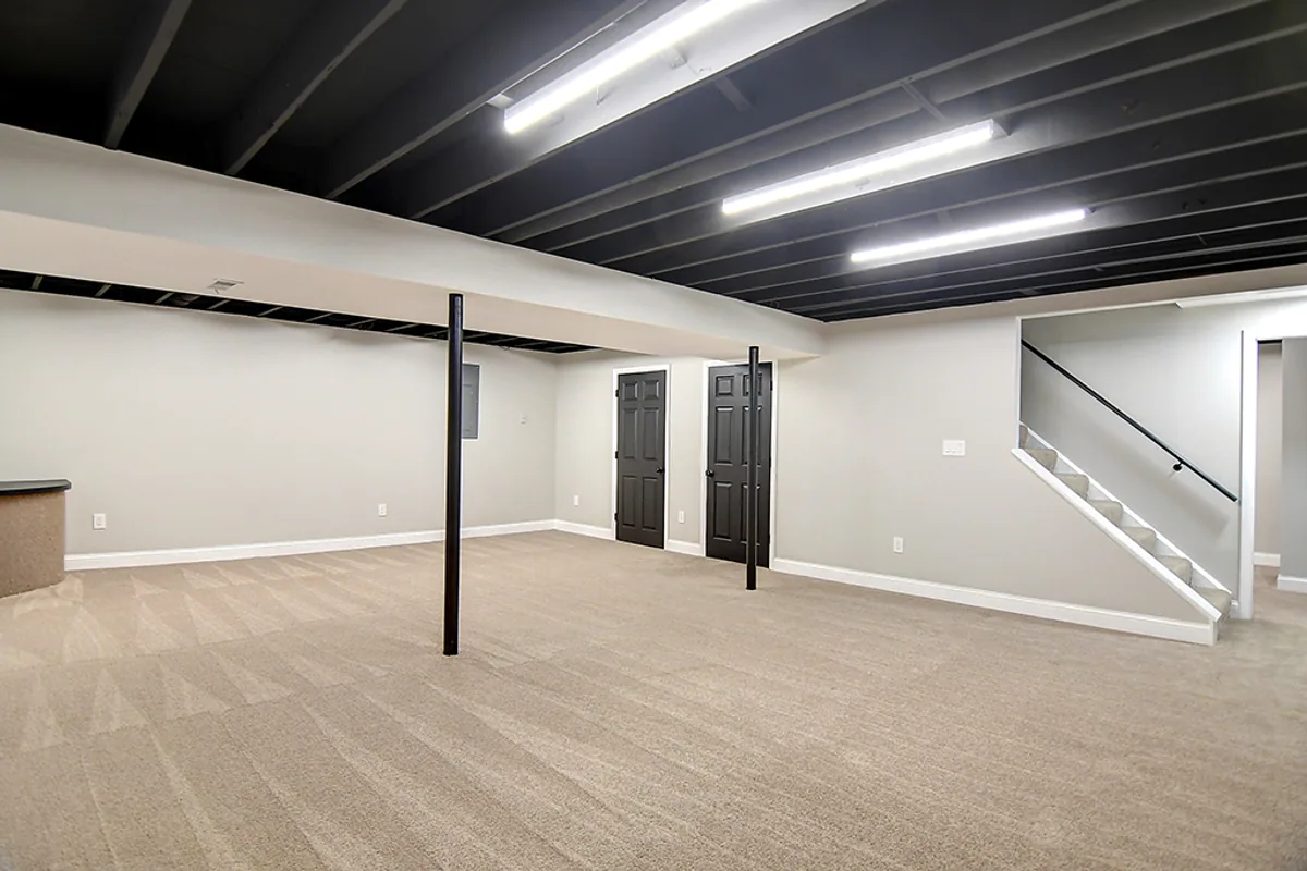Renovated Huber Heights finished basement after EZ Sell Homebuyers — exposed joists painted matte black, modern LED strip lighting, fresh carpet, open bonus room ready for rec, gym, or office use