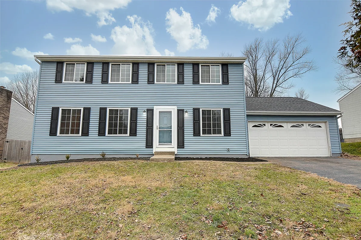 Same Huber Heights colonial on Chukar Drive after EZ Sell Homebuyers renovation — power-washed blue siding, fresh black shutters, clean landscaping, refreshed curb appeal