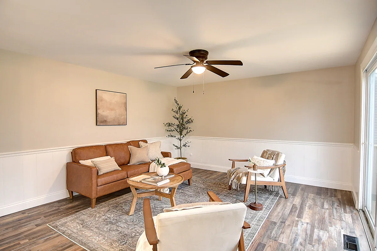 Renovated Huber Heights family room after EZ Sell Homebuyers — bright white wainscot, luxury vinyl plank, modern sofa, open sun-filled space with slider access