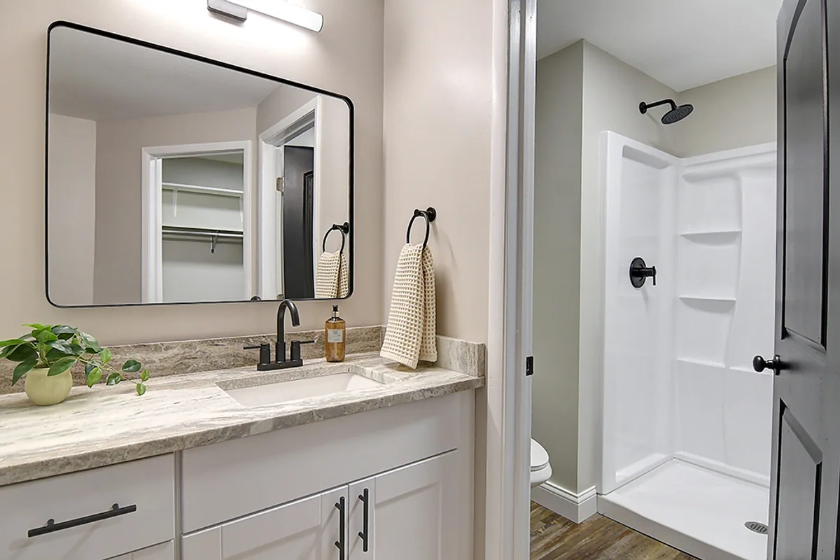 Renovated Huber Heights full bath after EZ Sell Homebuyers — granite-look vanity, modern wide mirror, matte black sconce and fixtures, clean white shower stall, refinished hardwood floors