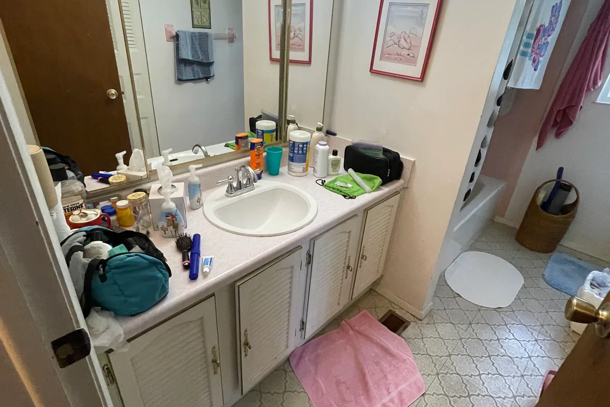 Huber Heights Chukar Drive full bath before EZ Sell Homebuyers — louvered double vanity, mirror panel wall, Hollywood light bar, dated tile floor, fiberglass shower with rust
