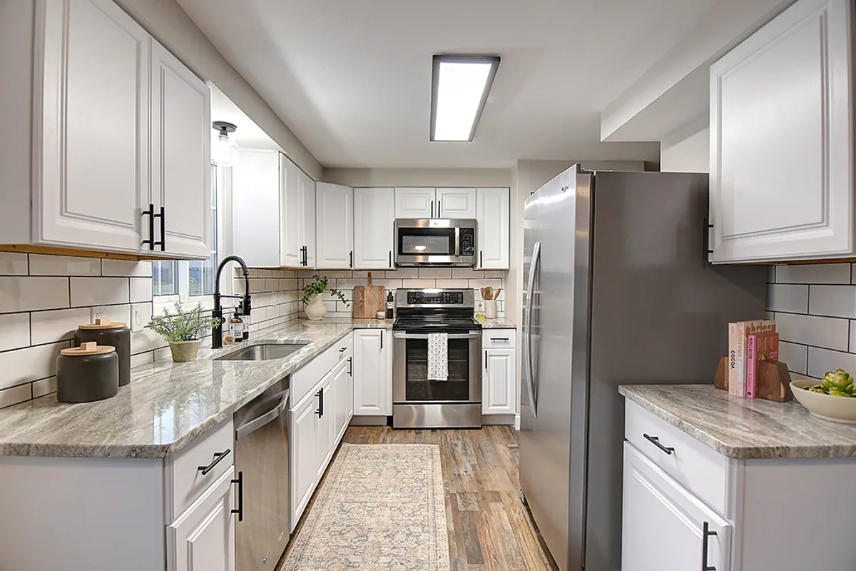 Renovated Huber Heights kitchen after EZ Sell Homebuyers — white shaker cabinets, granite countertops, subway-tile backsplash, stainless steel appliances, black gooseneck faucet