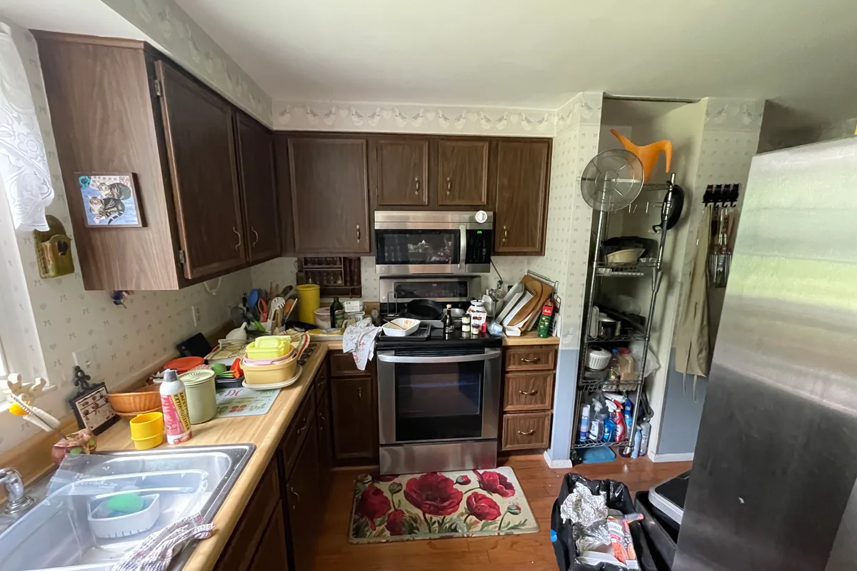Huber Heights Chukar Drive kitchen before EZ Sell Homebuyers cash purchase — original 1980s dark wood-laminate cabinets, wallpaper border, dated fluorescent lighting