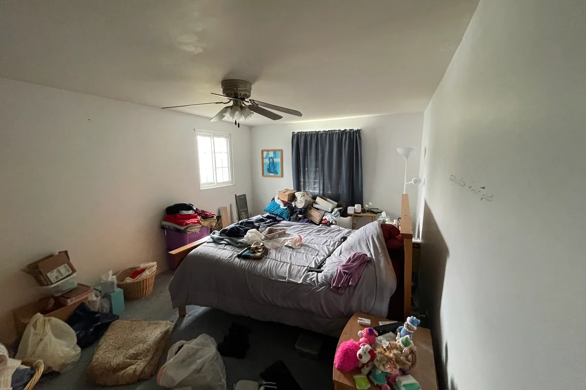 Huber Heights Chukar Drive master bedroom before sale — cluttered with boxes and storage, stained carpet, scuffed walls, dated ceiling fan