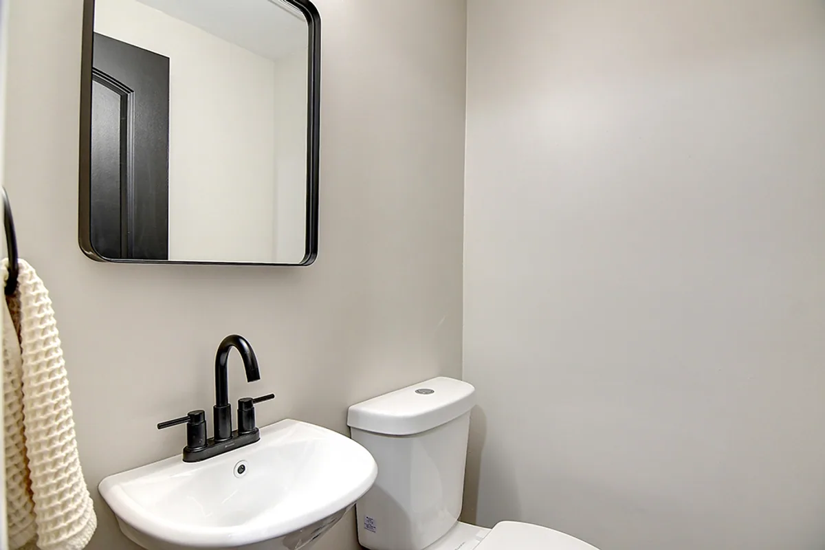 Renovated Huber Heights powder room after EZ Sell Homebuyers — fresh greige paint, wall-mount sink, matte black faucet, modern rounded mirror, clean floor