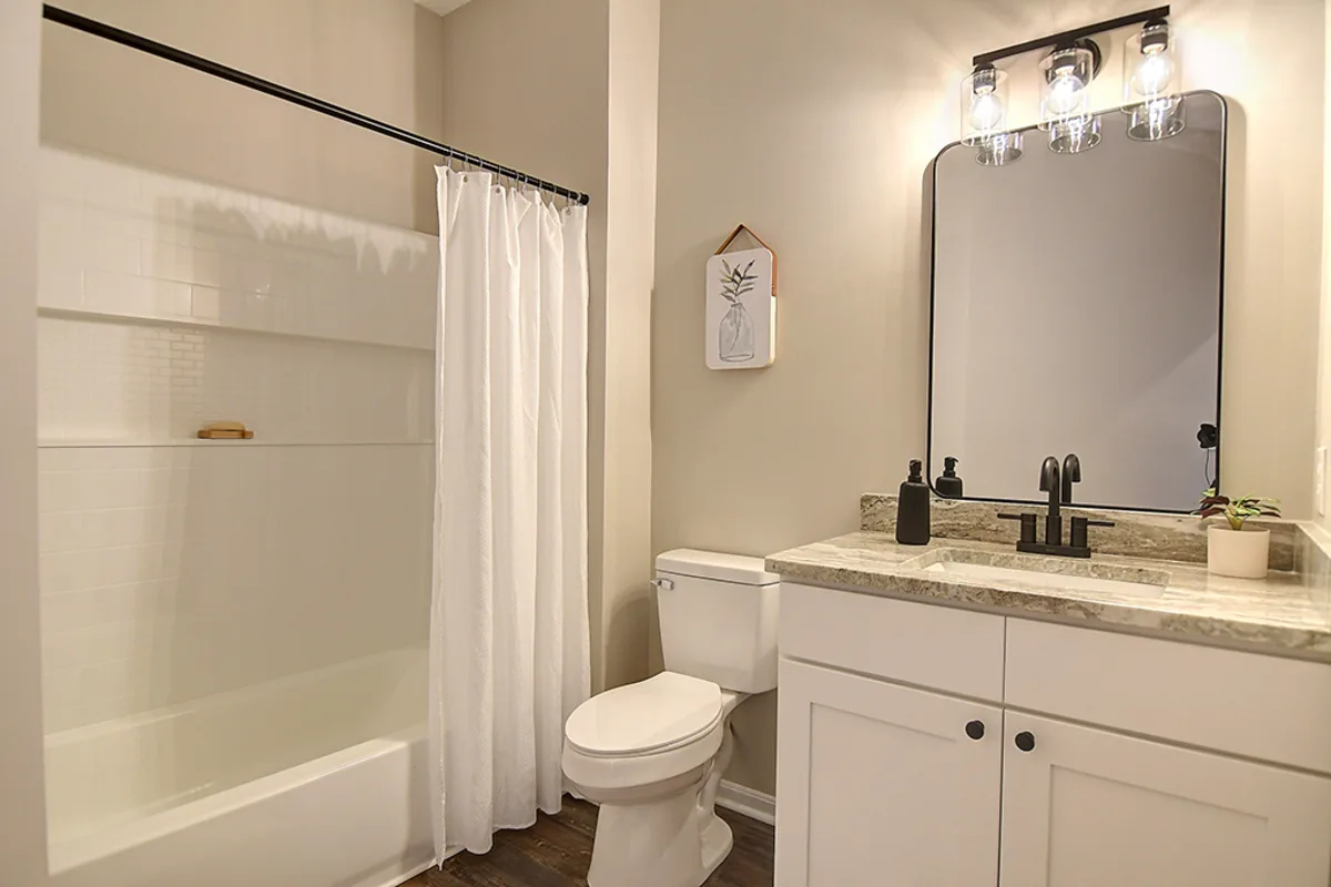 Renovated Miamisburg 1539 Commons Drive bathroom after EZ Sell Homebuyers — white shower stall, white shaker vanity, granite top, three-light black bath bar, matte-black fixtures, refinished flooring