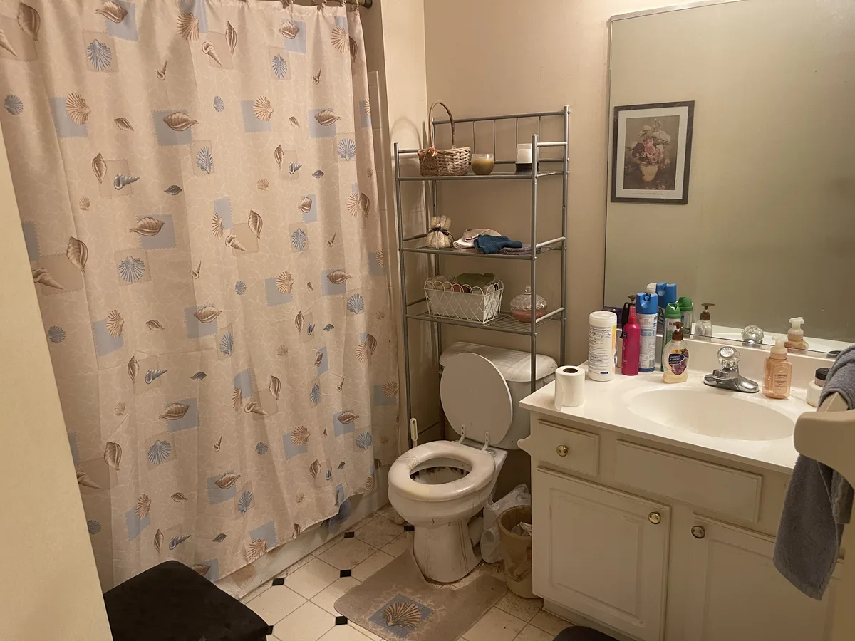 Miamisburg 1539 Commons Drive bathroom before EZ Sell Homebuyers — seashell shower curtain, dated vanity, brass knobs, dim sconce, tired tile floor