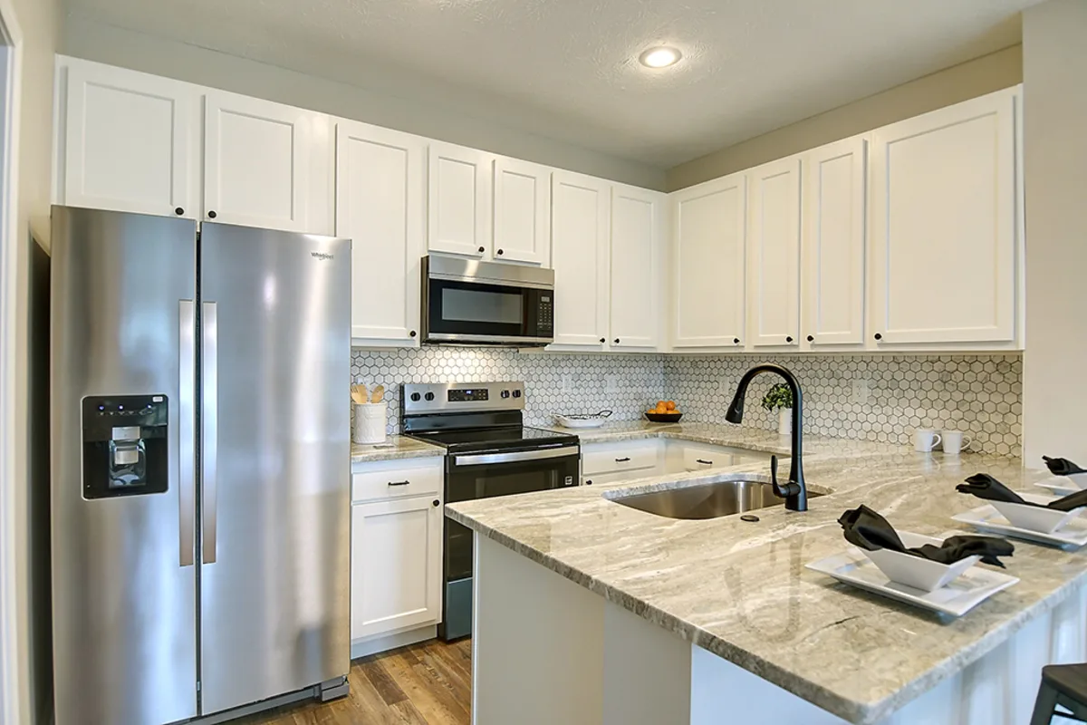 Renovated Miamisburg 1539 Commons Drive kitchen after EZ Sell Homebuyers — fresh white cabinets, granite countertops, hex-tile backsplash, stainless steel appliances, black gooseneck faucet, peninsula seating