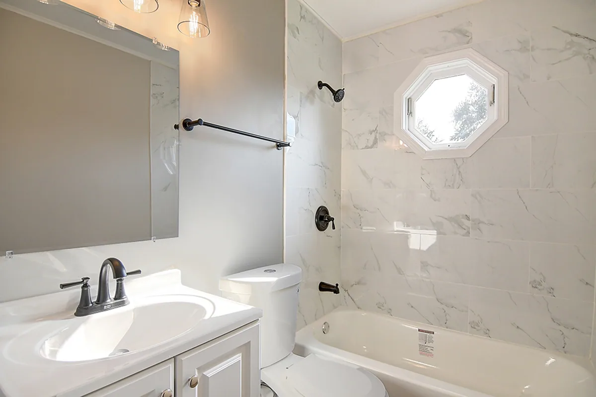 Renovated Fairborn bathroom after EZ Sell Homebuyers — marble look tile tub surround, new vanity with oil rubbed bronze fixtures, restored octagon window