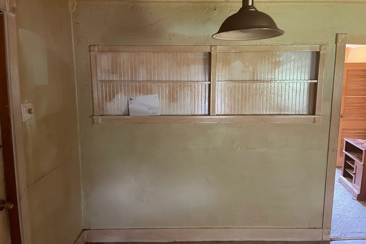 Fairborn Florence Avenue dining nook before sale — dated plaster built-in shelves, yellowed walls, vintage pendant light, worn rug