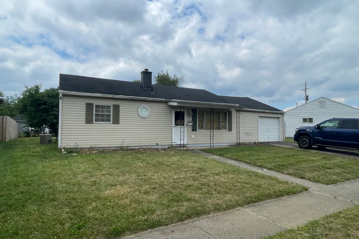 Fairborn Florence Avenue ranch before cash sale to EZ Sell Homebuyers — faded cream siding, overgrown landscaping, dated octagon window