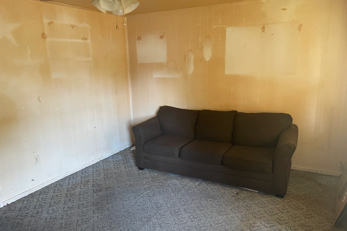 Fairborn Florence Avenue living room before sale — yellowed wood paneling with patched holes, dingy carpet, dated brown sectional