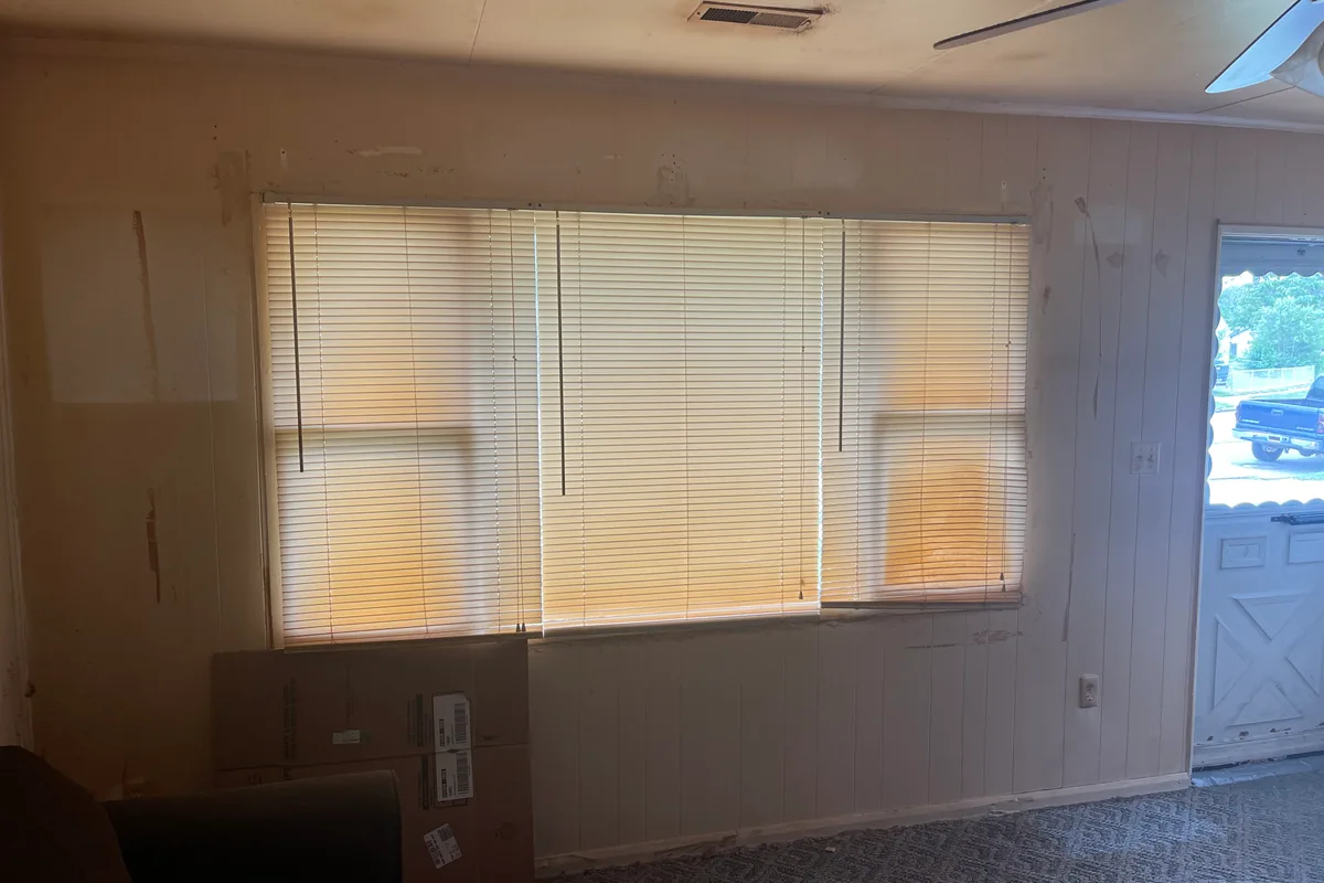 Fairborn Florence Avenue picture window wall before sale — sagging mini blinds, dated paneling, cardboard boxes, dim natural light