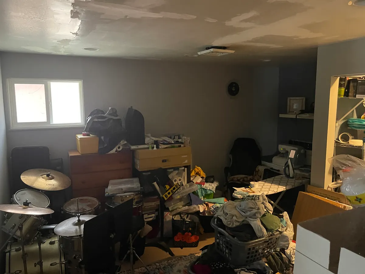 Kettering Utica Drive converted garage before EZ Sell Homebuyers — water stained ceiling tiles, cluttered storage, drum kit, deferred repairs