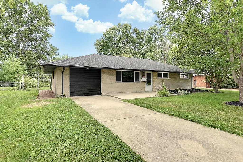 Same Kettering brick ranch on Utica Drive after EZ Sell Homebuyers renovation — fresh landscaping, painted garage door, summer curb appeal