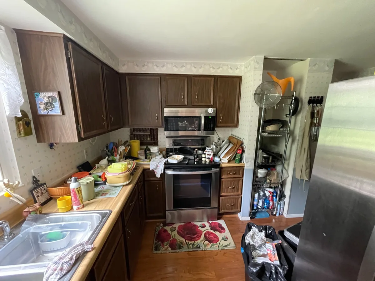 Kitchen before — dark brown cabinets, cluttered counters, dated wallpaper border